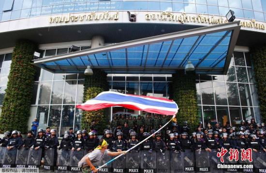 资料图：5月9日，泰国一名反政府示威者在防暴警察和士兵把守的泰国曼谷国家电视台NBT前挥舞国旗示威。