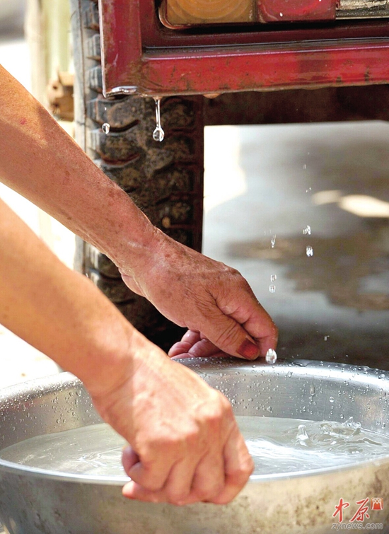 村民董粉用盆在老伴刚刚拉水的三轮摩托车下接洒落的水。