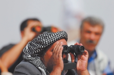 13日，在土耳其桑利乌尔法省的叙吕奇，人们用望远镜观察叙利亚城镇科巴尼的情况。叙利亚空军当天向叙中部与北部反对派武装据点进行了40轮空袭。