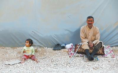 10日，在土耳其桑利乌尔法省叙吕奇镇一难民营，一名叙利亚库尔德男子和一名儿童坐在帐篷旁。