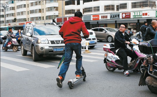 　　一市民滑着新奇的电动滑板车过街，吸引了路人好奇的目光  郎晓伟