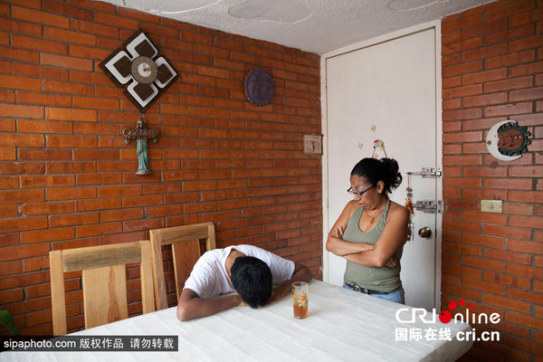 图为球队队长Baruch在伊斯塔帕拉帕区的家中，他趴在桌子上，旁边是他的母亲。