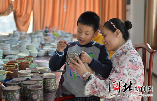 小学生在家人的指导下体验制作景泰蓝工艺品。