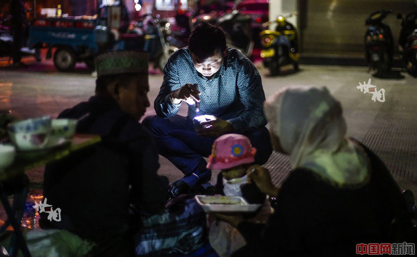 3月9日晚，一位缅甸宝石商人在云南省瑞丽市德龙珠宝夜市里给自己孩子喂饭。