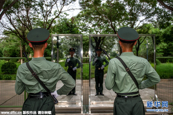 图为两名持枪战士对着镜子进行站军姿训练，衣服早已被汗水湿透。