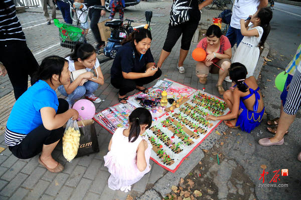 这位大姐将小摊摆在广场门口，立刻吸引了很多家长和孩子的围观。