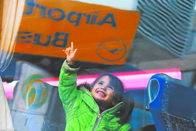 6日，在德国慕尼黑火车站外的难民集合区，一名乘坐大巴前往难民临时安置点的小女孩在向外挥手。