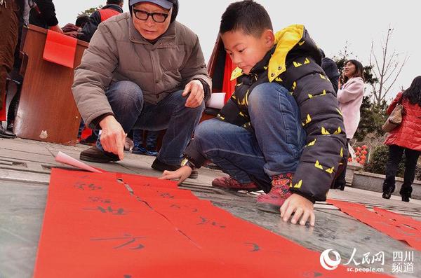 送春联是年画节的一个重要活动,一位小孩在爷爷的带领下,将免费领取的春联放在地上。(刘浏 摄)