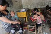 2012年5月18日，河南省洛阳市嵩县艾力希望小学，代课老师刘花花抱着学前班两岁半的张仕豪，指导其他孩子们趴在桌子上午休。