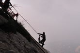 华山东峰悬崖边，几名环卫工正在放绳下崖。