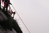 华山东峰悬崖边，几名环卫工正在放绳下崖。