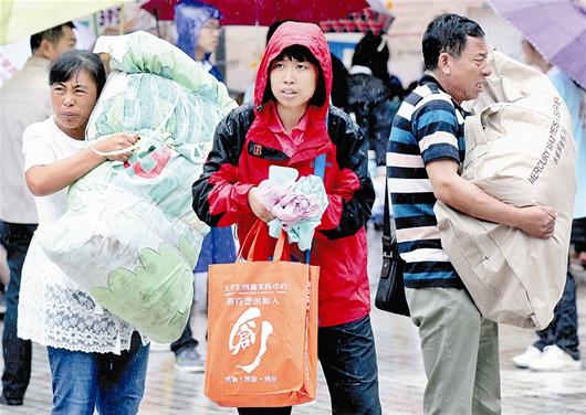  图为：细雨中，父母帮孩子抱着行李步入校园
