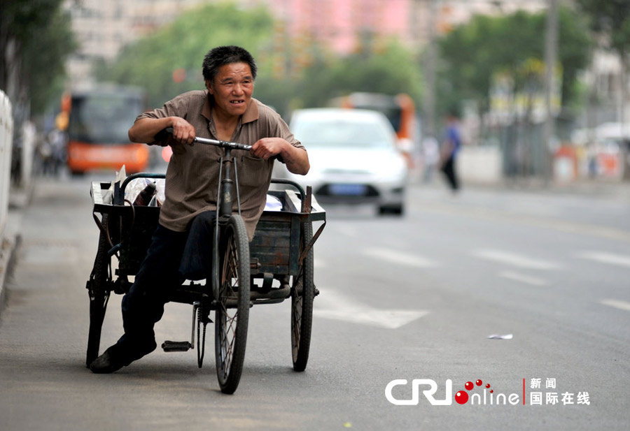 独腿“破烂王”用一条腿蹬地，驾驶三轮车在路边捡拾能换钱的废品。图片来源：CFP