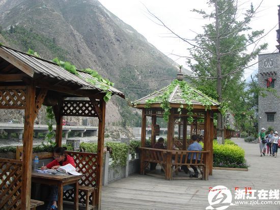 岷江畔的民俗景观带一景。木质地板,木质亭榭,羌式房屋。 这休闲景观带,恰是独一无二的民俗街,长长的木栈道,点缀着一个个亭台楼榭;外侧是奔腾的岷江,内侧是小桥流水建筑,大型仿真水车群和羌族农具、座椅、餐馆等相映成趣。漫步的游人,亭内悠坐的老人、看书的姑娘,闲适舒心。好一幅灾区变景区,家园变花园,农民变市民,人民安居乐业,人与自然和谐相处的图画。徜徉其间,顿觉否极泰来,太平盛世,其喜洋洋…… 废物利用好景观,旧木翻新成特色!这民俗景观带有个独特的木景,木质的羌寨,木质的